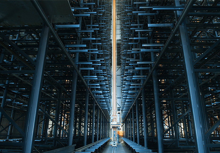 ASRS 1 Long warehouse aisle between tall blue metal storage racks reaching up to the ceiling.