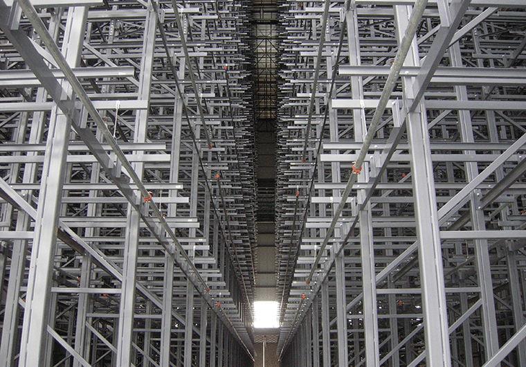 ASRS 4 Long aisle between tall grey metal pallet racks in a vast warehouse, viewed from end toward light.