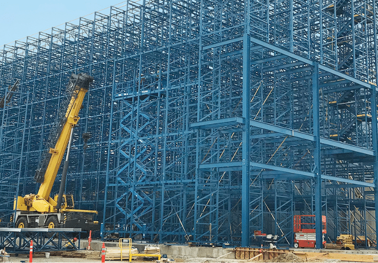 ASRS 5 Blue steel scaffolding framework under construction with a yellow mobile crane on the left at a site.